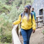 solo woman traveler in yellow jacket walking along mountain path