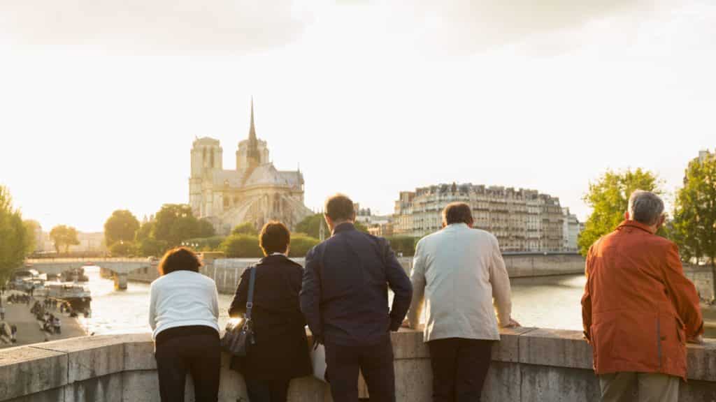 A group of seniors on a European tour enjoying the view from a bridge in Paris