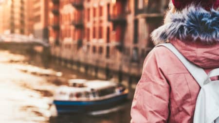 Rear crop view of adult woman tourist with backpack enjoying tourist river pleasure tour boat in Speicherstadt historical warehouse district in golden sunset light. Hamburg, Germany, Europe on tour