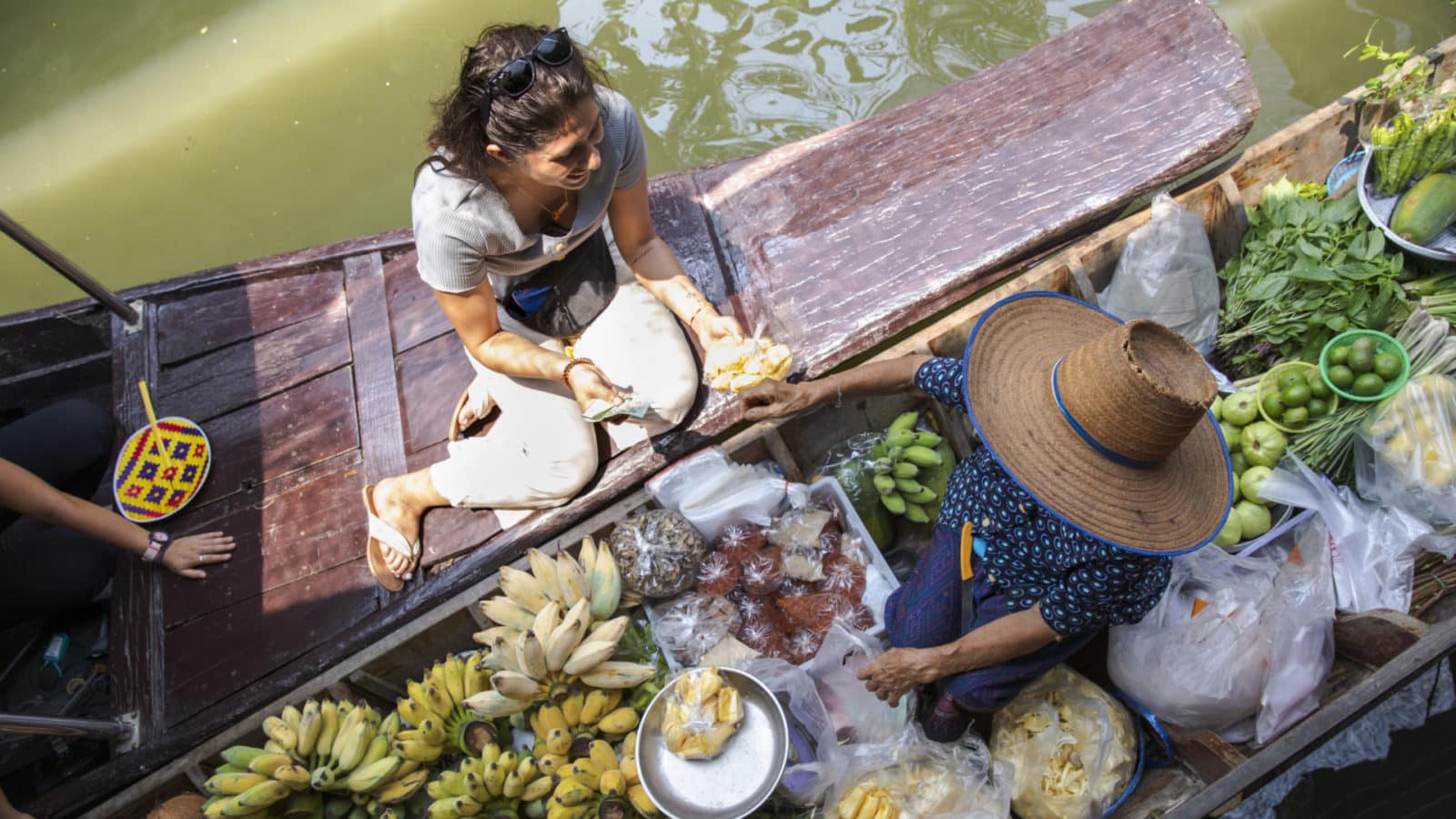 female tour traveler buying fruit from a floating market boat in Bangkok, Thailand
