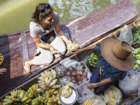 female tour traveler buying fruit from a floating market boat in Bangkok, Thailand