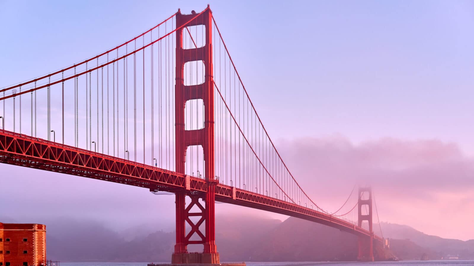 view of the Golden Gate bridge and Fort Point at sunrise with light fog