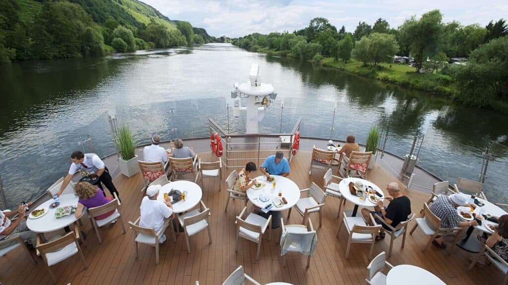 People dining onboard a Viking River Cruise ship with beautiful water and forest in the background