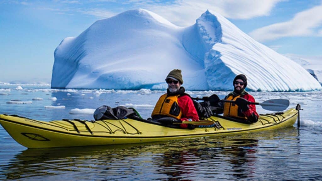 two people kayaking with icebergs in the background on an Intrepid tour