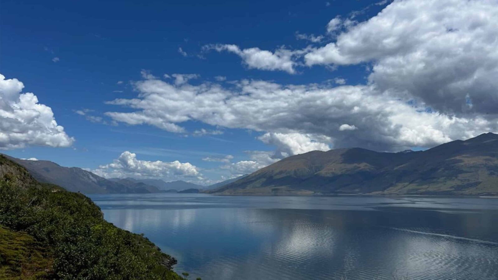 View of water and mountains with puffy clouds and blue skies on Adventures by Disney tour in New Zealand