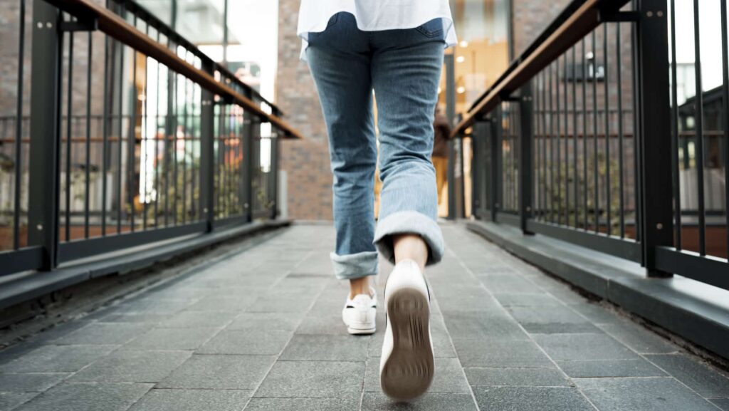 Back view of a woman in jeans and sneakers walking in the street, close up