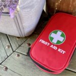Travel first aid kit next to backpack and small bouquet of lavender on park bench