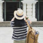 Solo tour traveler wearing a hat, a backpack, and a striped shirt taking a photo while traveling