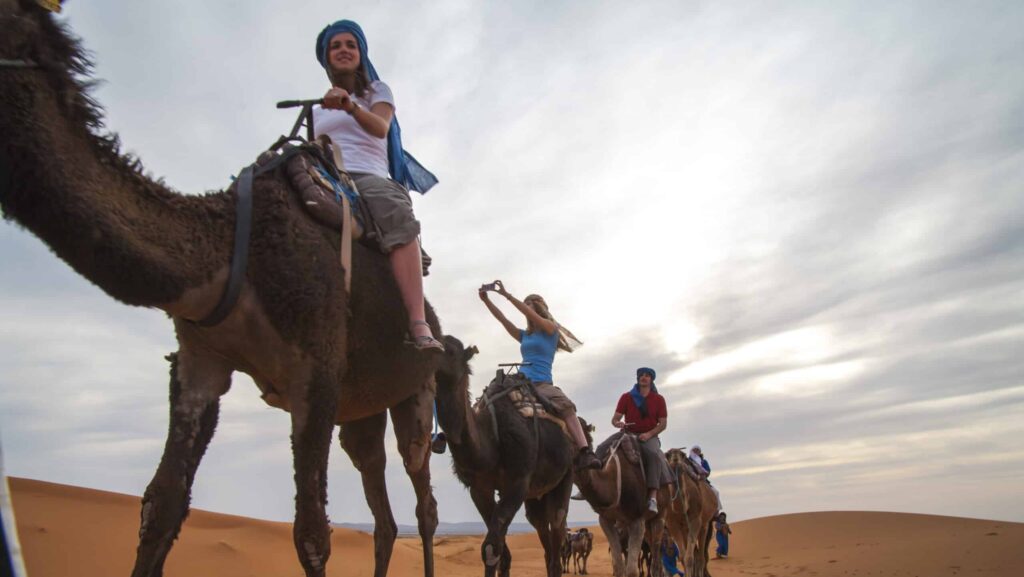 G Adventures tour guests riding camels through Morocco's Sahara Desert