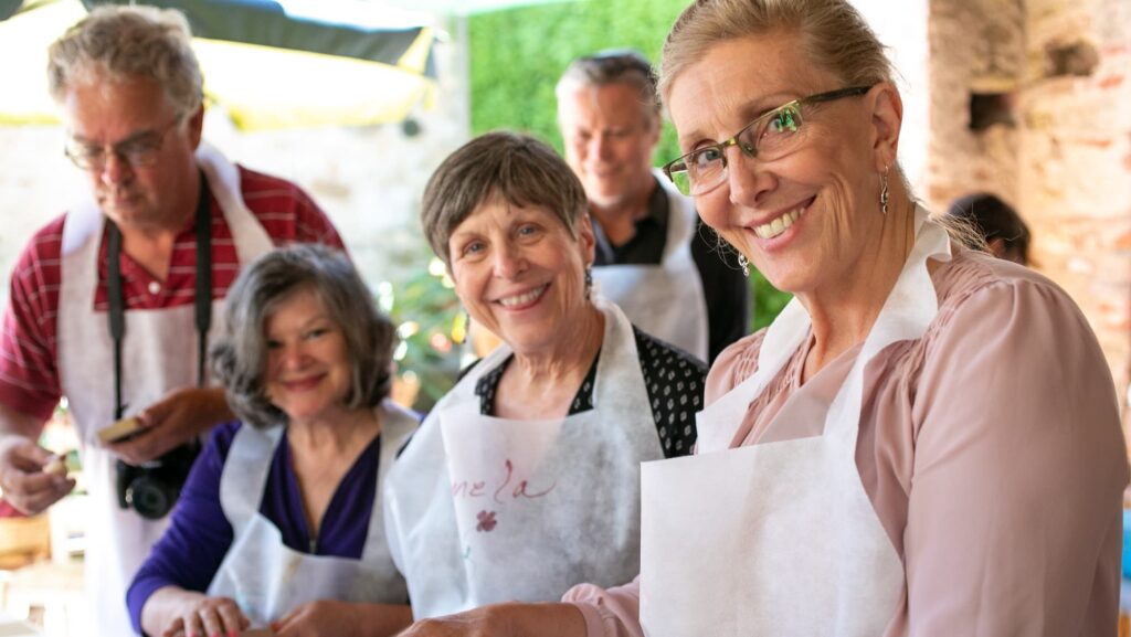 Road Scholar participants in aprons cooking during the Cooking in Tuscany program. Participants enjoy an afternoon of cooking outdoors at the International Academy of Italian Cuisine with Director Gianluca Paradini with ingredients purchased at a local farmers market