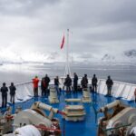 Intrepid trip to Antarctica, with people on the bow of the ship looking out at icebergs