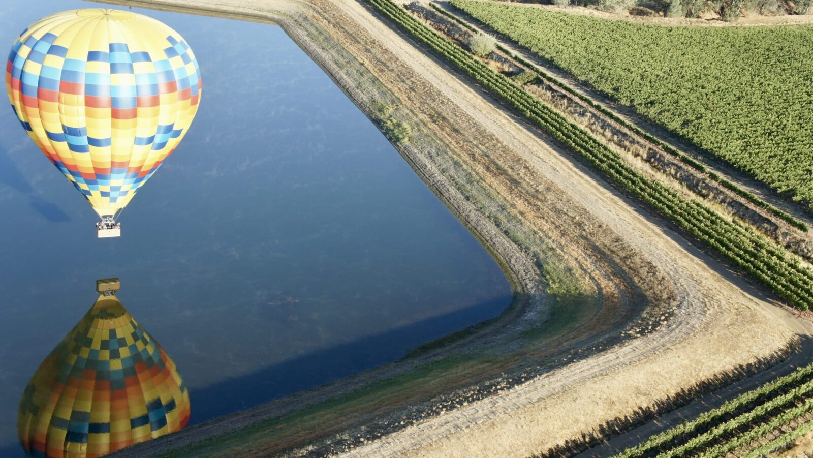 view of hot air balloon reflected in a pond, from the vantage point of a higher hot air balloon