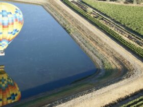 view of hot air balloon reflected in a pond, from the vantage point of a higher hot air balloon