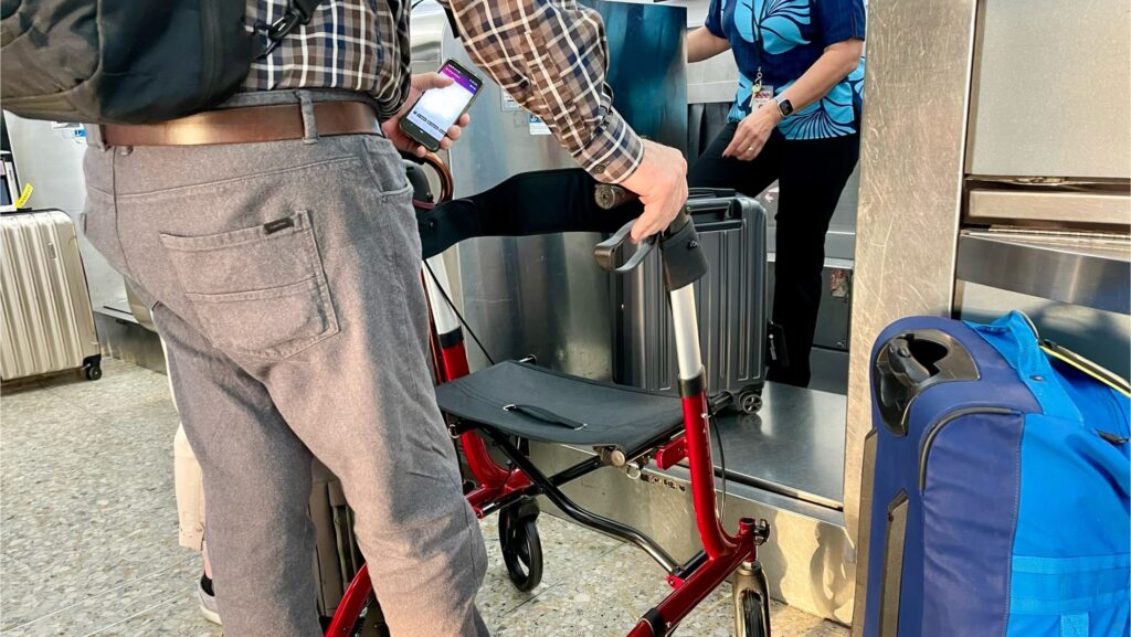 close up of man standing at airport check in desk with his walker and suitcase