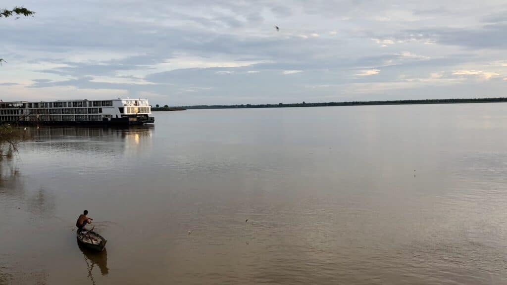 View of the Mekong River and an Avalon waterways ship with traditional fishing boat and fisherman in foreground