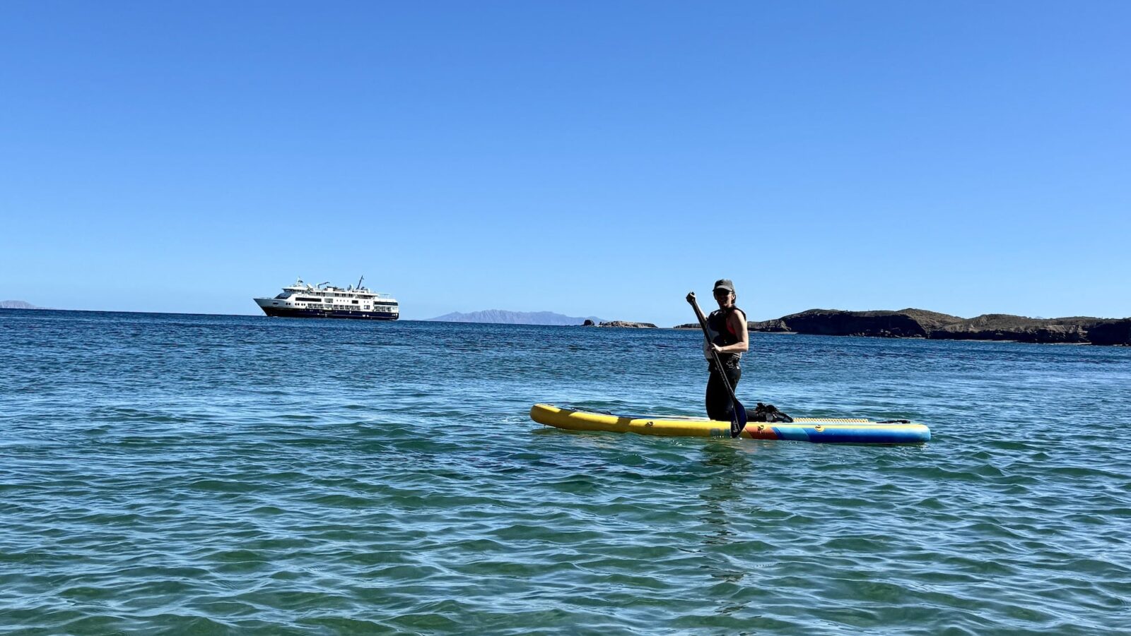 Person stand up paddleboarding with the National Geographic Venture in the background