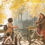 Friends with bicycles along sunny autumn canal in Amsterdam
