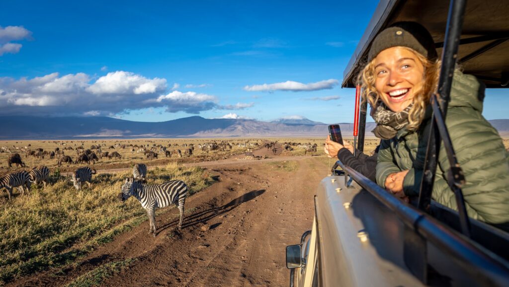 person looking out safari truck and laughing with zebras and savannah in background