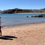 tour director and tour traveler looking out on water along a beach