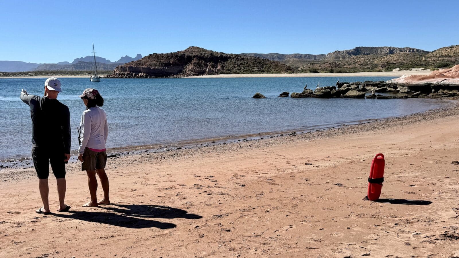 tour director and tour traveler looking out on water along a beach