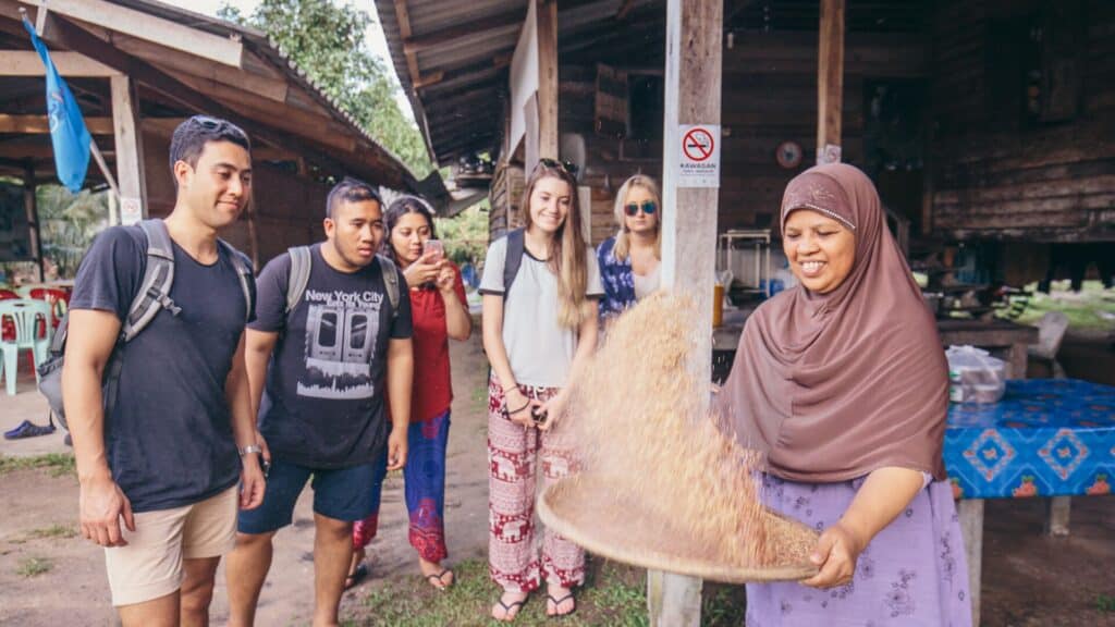 Young travelers on Intrepid Travel's 18 to 35s trip to Thailand, watching a local prepare rice in Krabi