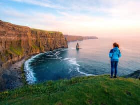 Woman standing on a grassy hilltop edge overlooking the ocean and vertical cliffs