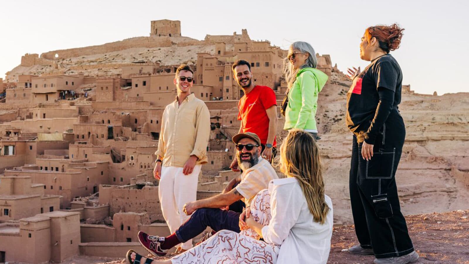 People standing on top of a hill overlooking a ledge with buildings built into its side