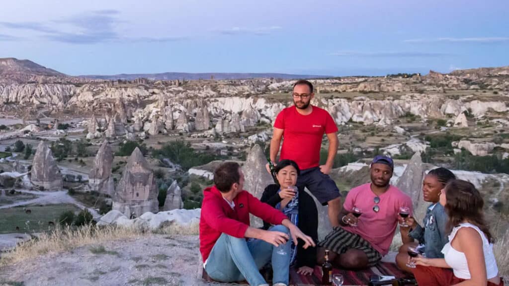 Travelers sitting and drinking wine on top of a mountain with unique geological formations in the background