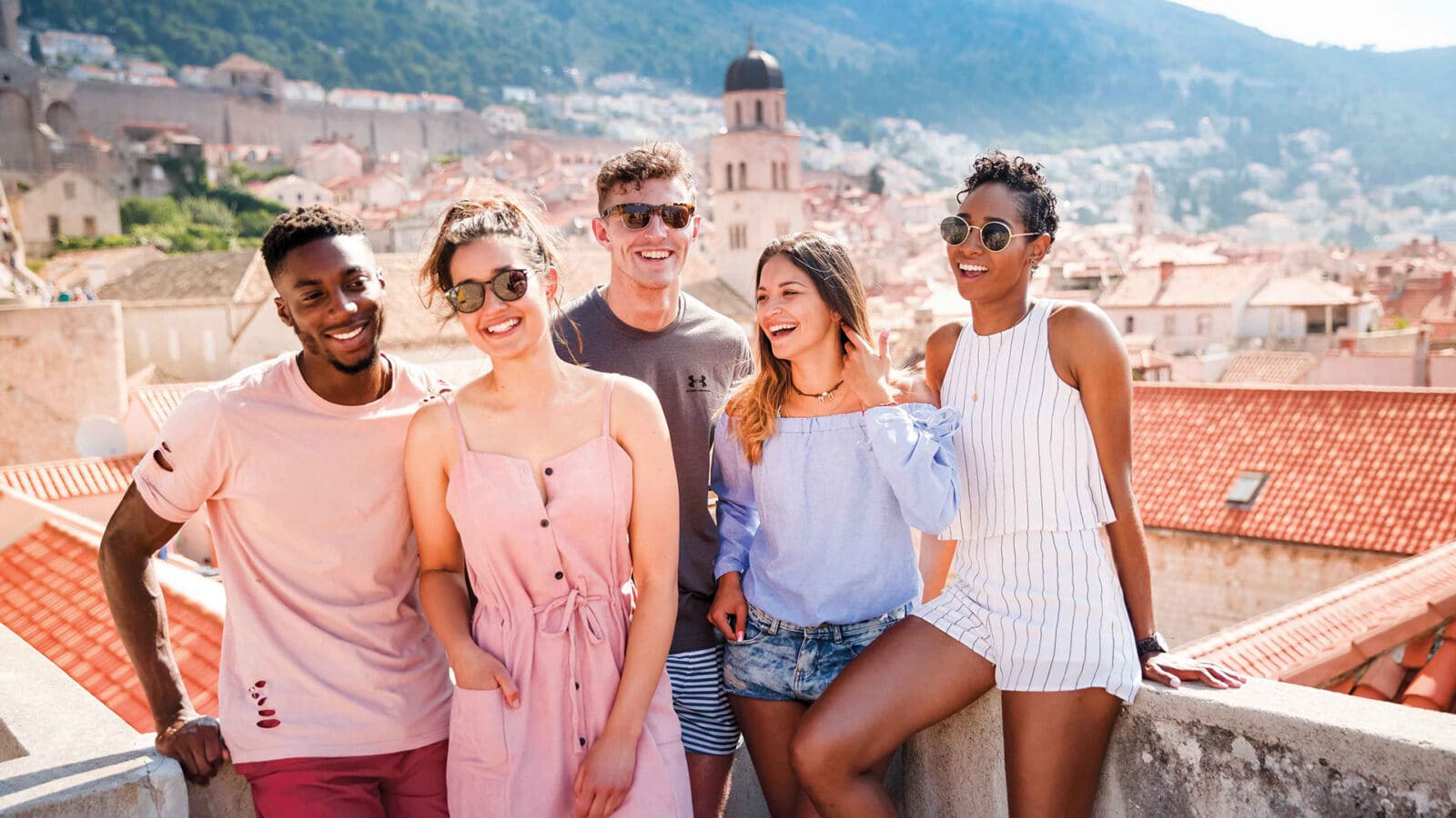 Young adults standing on a rooftop with an ancient city and mountains in the background