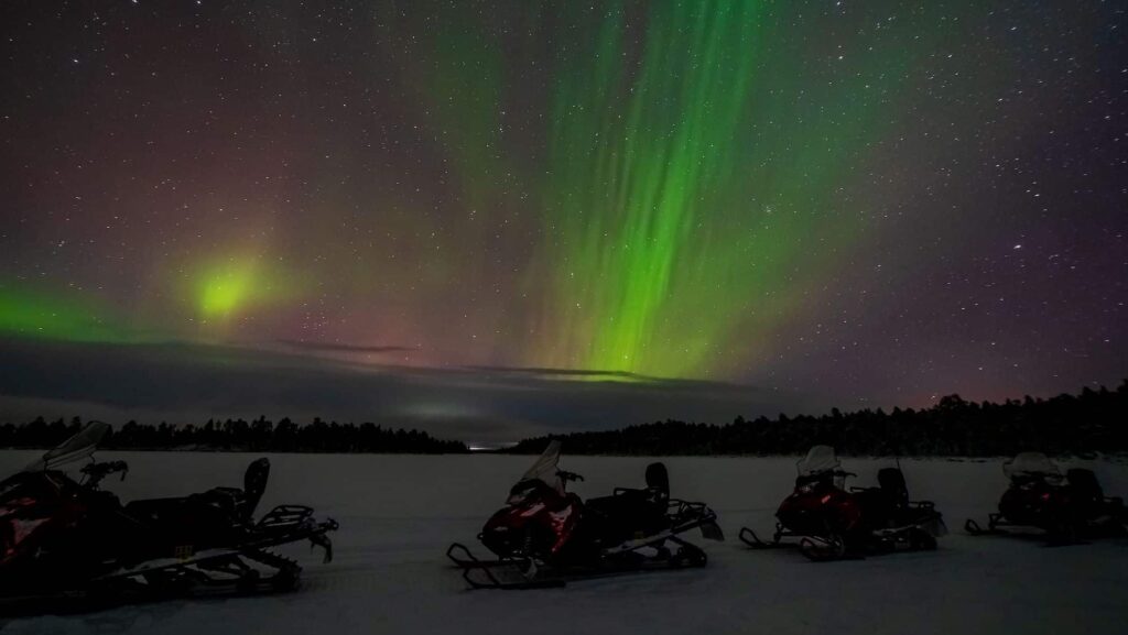 Northern lights in the distance and snowmobiles in the foreground