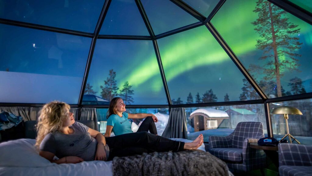 Two women looking at the Northern Lights from a glass dome at Findland's Levin Iglut hotel during a Backroads tour