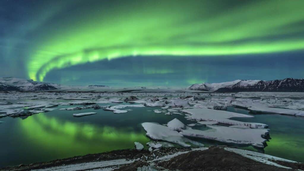 The Northern Lights in blue and green in Jokulsarlon over an icy body of water