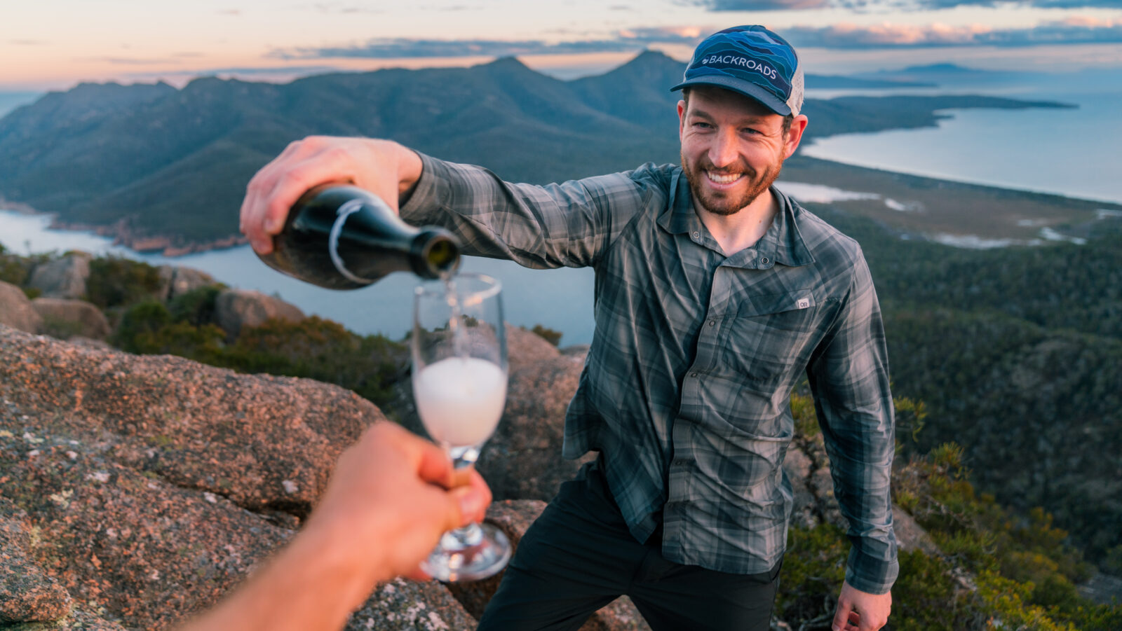 man pouring glass of sparkling wine with dramatic scenery behind