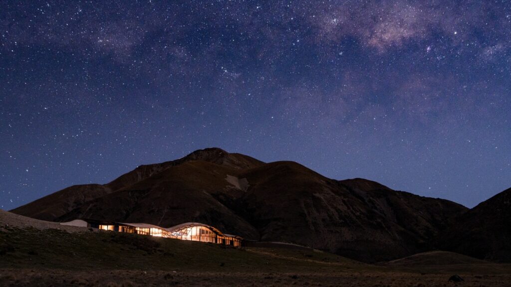 A starry night sky over a rocky outcrop and illuminated hotel in New Zealand