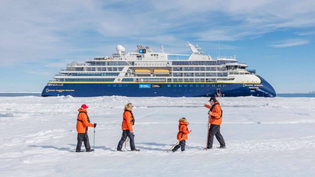 Guests of multiple ages walking on the fast ice in the Weddell Sea with the National Geographic Resolution ship behind them