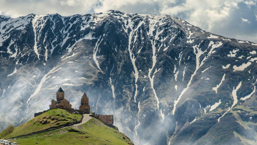 Buildings on a green hill in front of snowy mountains in the country of Georgia
